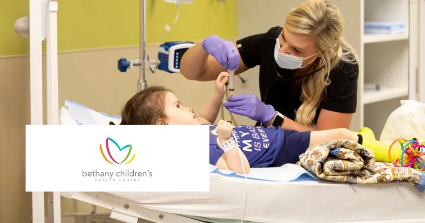 A healthcare worker in a mask and gloves tends to a child on a hospital bed. The logo reads "Bethany Children's Health Center."