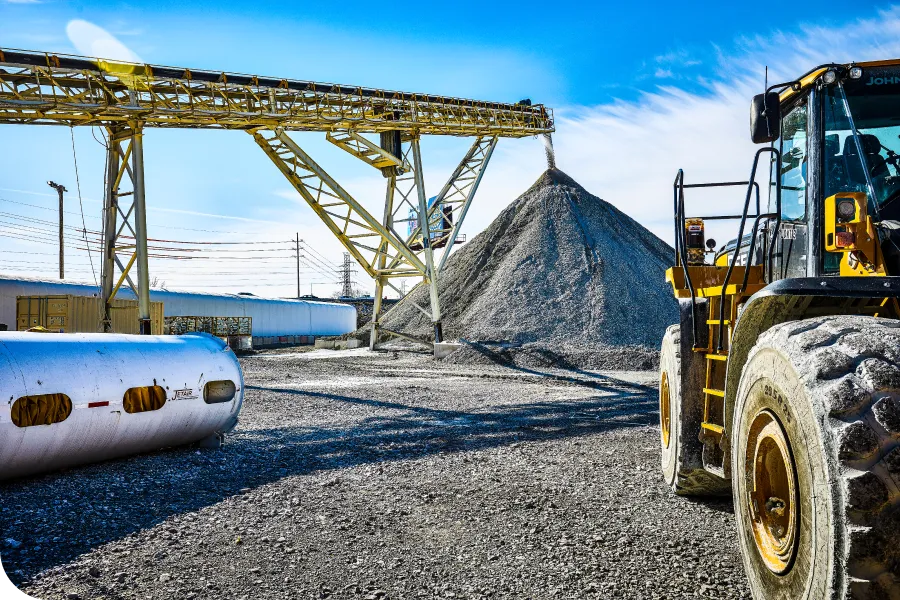 Construction site with a large pile of gravel, a conveyor belt, and a yellow front loader under a clear blue sky.