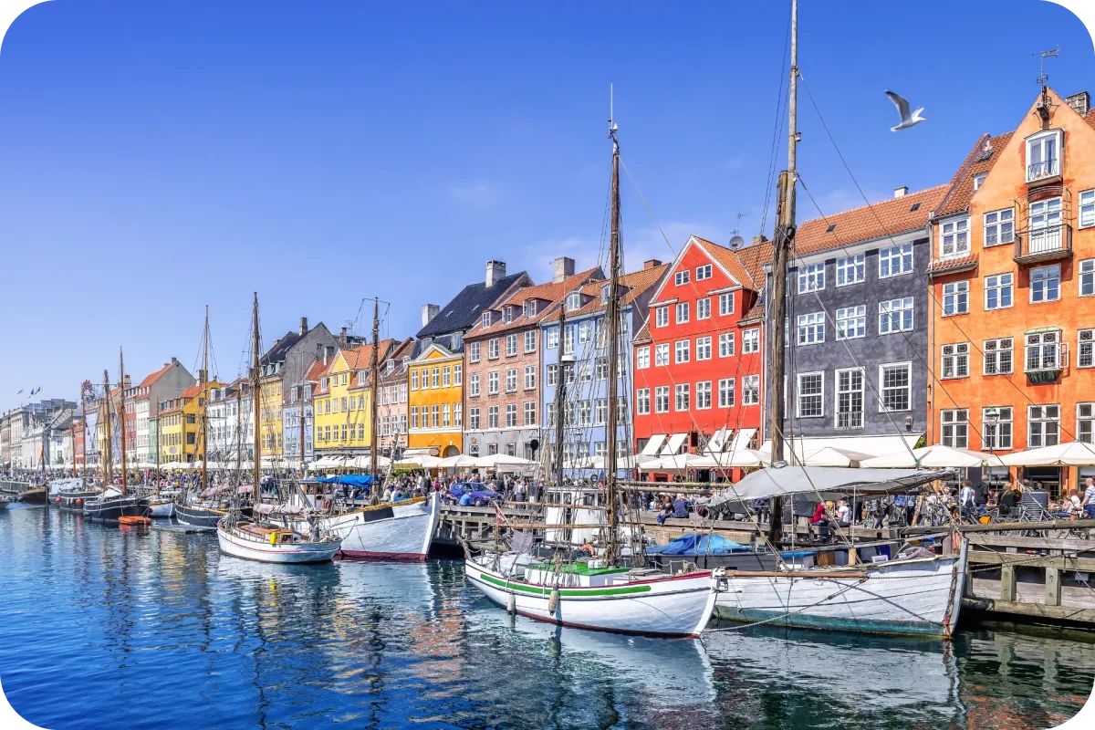 Colorful buildings line the waterfront at Nyhavn in Copenhagen, with boats docked along the canal under a clear blue sky.