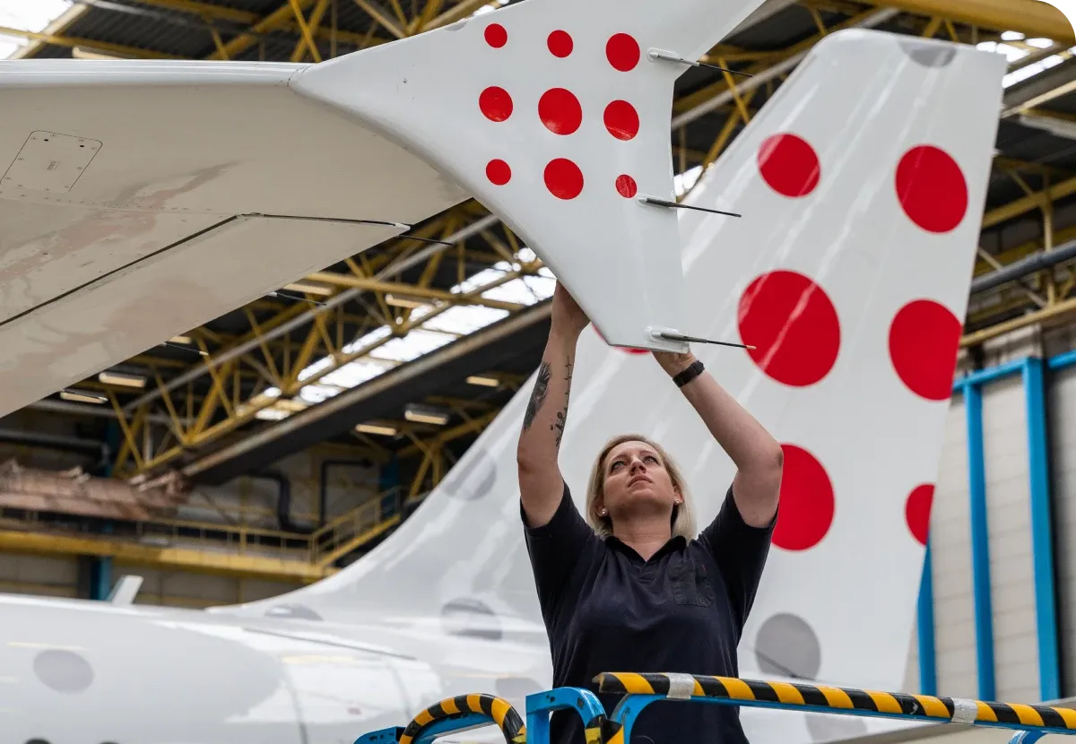 Technician inspects the tail of an aircraft with red polka dots in a hangar, standing on a platform.
