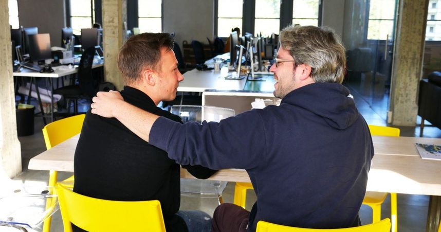 two men embrace each other in a friendly manner in an office setting