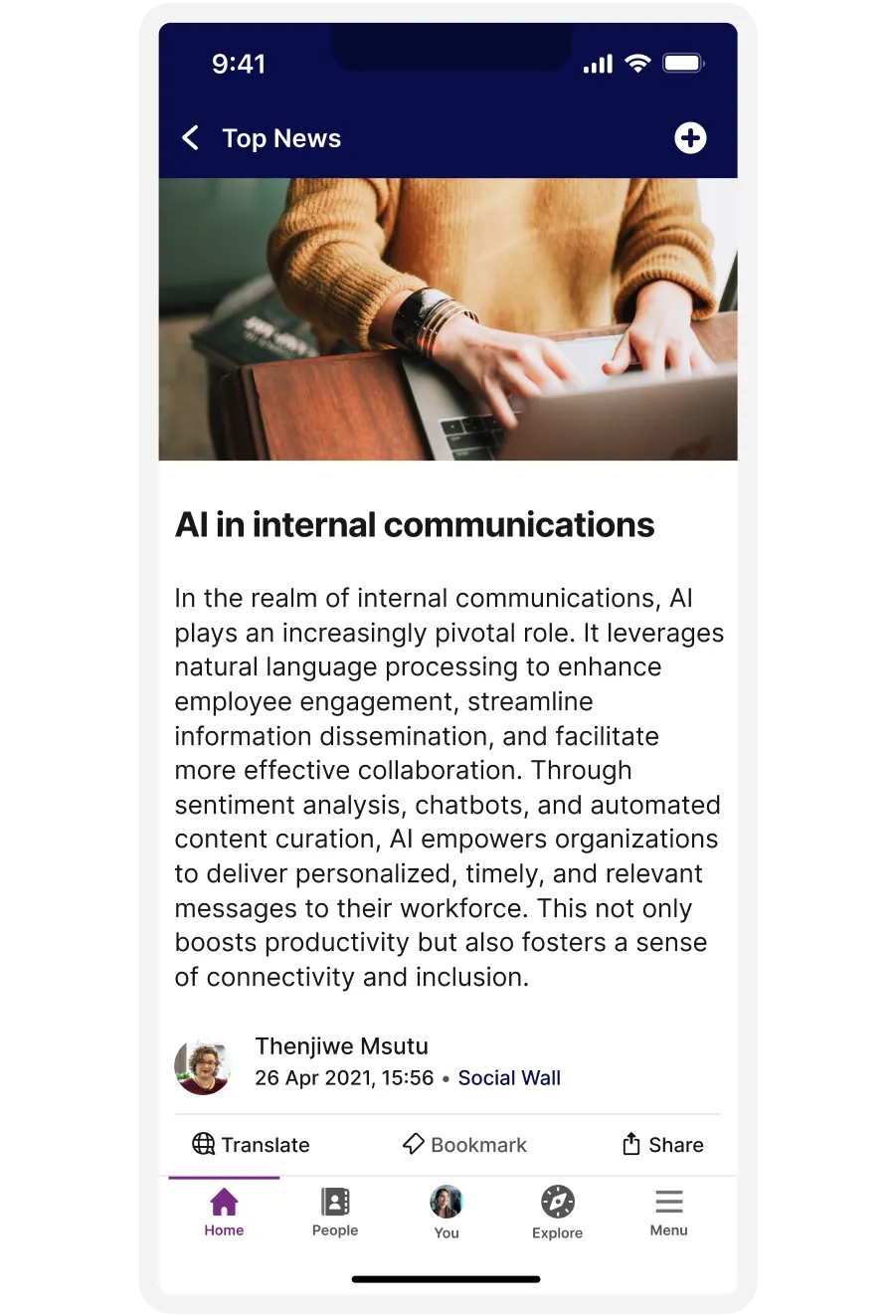A person using a laptop, with an article on AI in internal communications displayed on a smartphone screen.