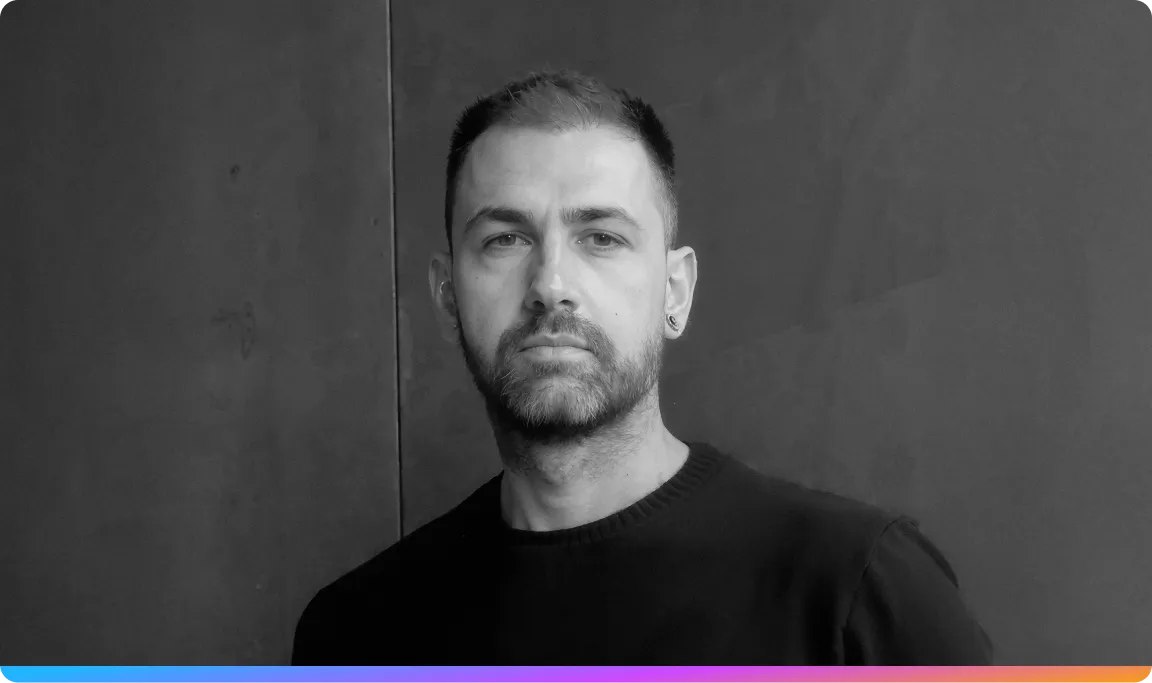 Black and white portrait of Giovanni Luperti with short hair and a beard, wearing a dark sweater, standing against a textured wall.