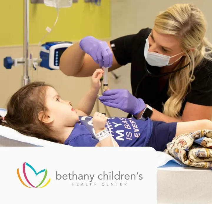 A nurse in gloves and a mask checks a young girl's reflexes in a hospital bed. The girl wears a purple shirt. Logo: Bethany Children's Health Center.