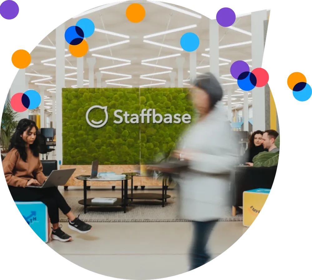 Modern office lobby with a green wall displaying "Staffbase." People are sitting and walking, some using laptops. Bright, colorful circles overlay.