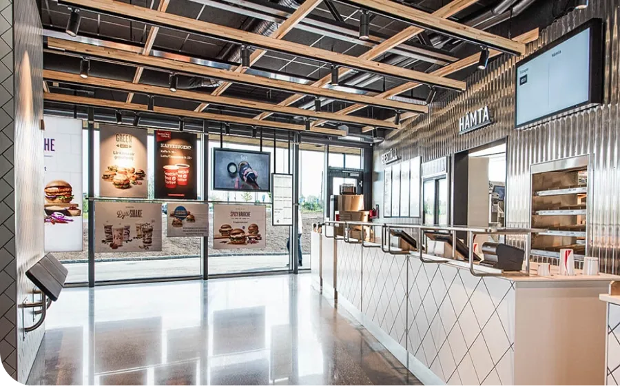 Modern fast-food restaurant interior with a sleek counter, digital menu boards, and large windows letting in natural light.