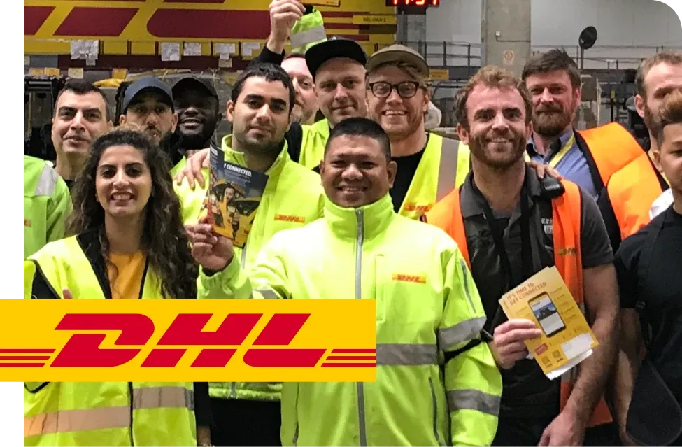 A group of DHL employees in high-visibility jackets smiling and holding promotional materials inside a warehouse.