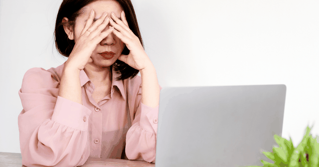 woman covers face while facing a laptop, image of apparent frustration