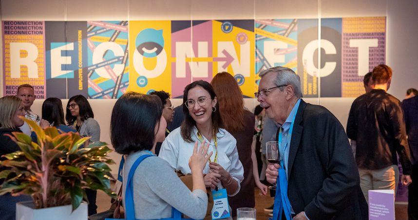 A group of internal communicators enjoy drinks and laughs at Staffbase's VOICES event in New York City. The background graphic behind them on the wall says "Reconnect".