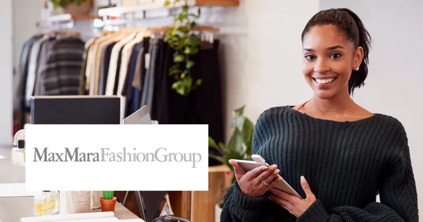 Smiling woman in a clothing store holding a phone, with racks of clothes in the background and a MaxMara Fashion Group logo.