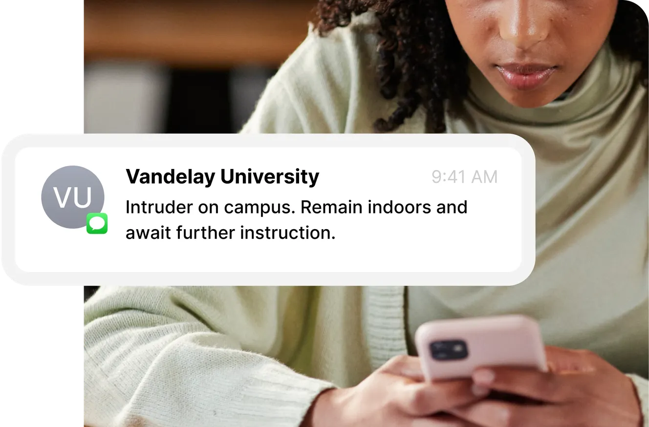 Person looking at a phone displaying a message from Vandelay University about an intruder on campus, advising to remain indoors.