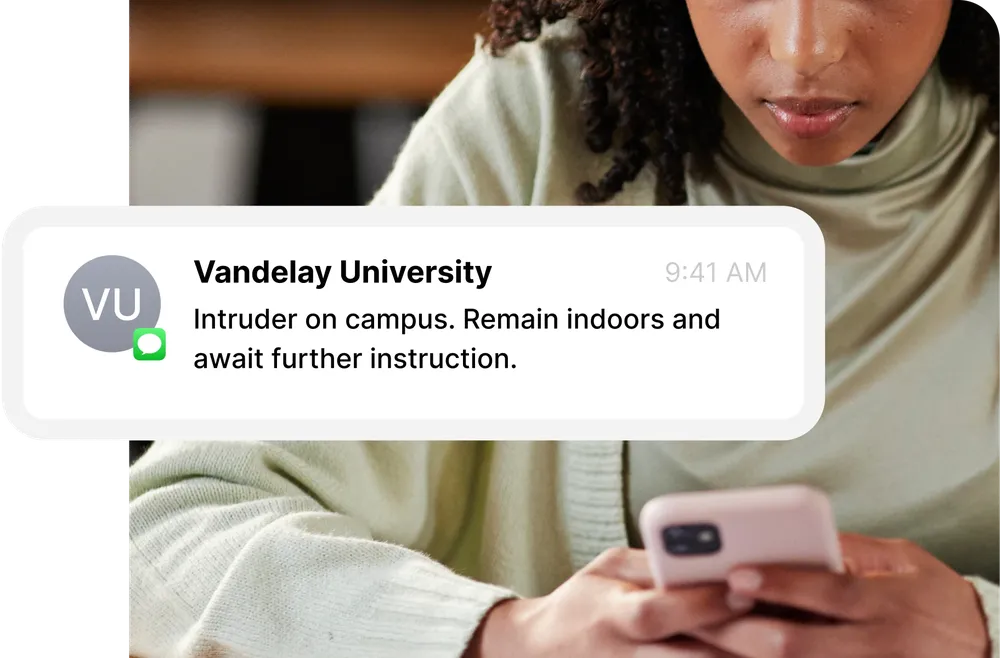 Person looking at a phone displaying a message from Vandelay University about an intruder on campus, advising to remain indoors.
