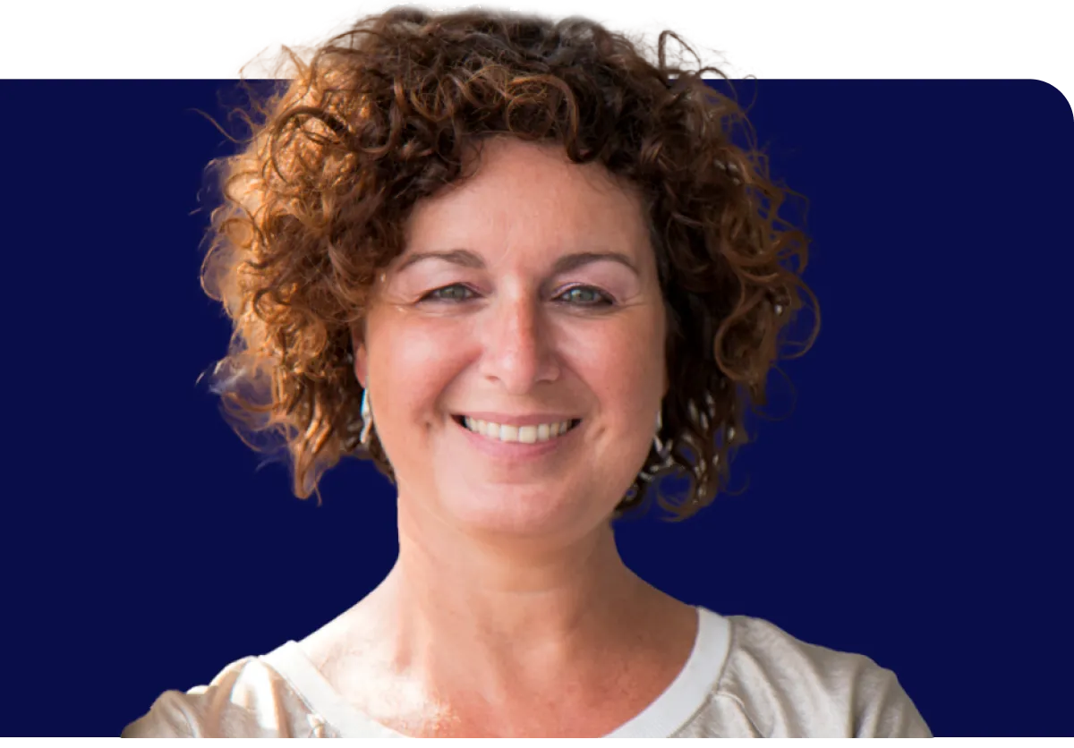 Smiling person with curly hair, wearing a light-colored top, against a dark blue background.