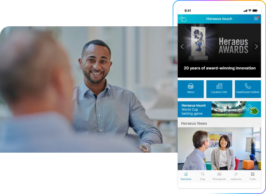 Man smiling in an office setting, with a smartphone screen displaying the Heraeus employee app interface on the right.