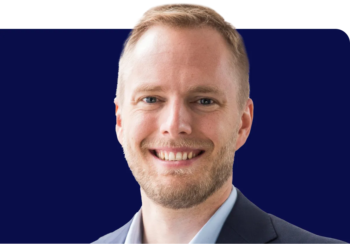 Smiling man with short hair and beard, wearing a suit, against a dark blue background.