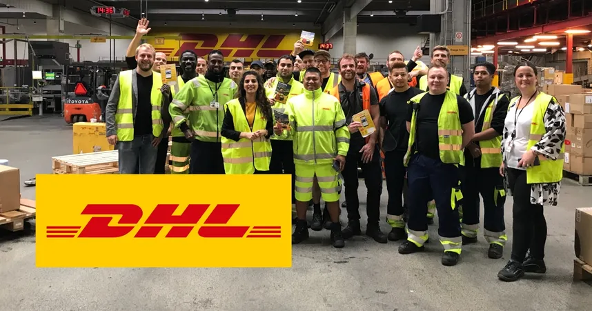 A group of DHL employees in high-visibility clothing smiling and posing in a warehouse, with DHL logo prominently displayed.