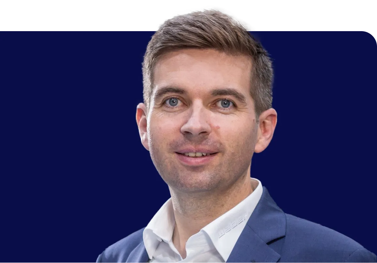 Man in a blue suit and white shirt smiling against a dark blue background.