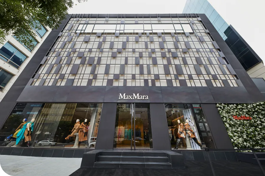 Exterior of a Max Mara store with mannequins in the window displays and a modern, geometric facade.