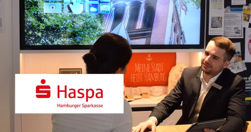 A man in a suit talks to a woman at a desk in a Haspa bank branch, with a screen and promotional materials in the background.