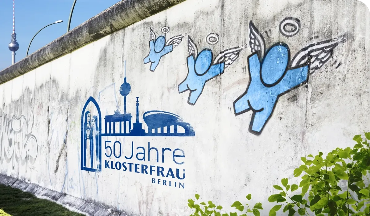 Graffiti of blue winged figures and "50 Jahre Klosterfrau Berlin" on a concrete wall, with the Berlin TV Tower in the background.