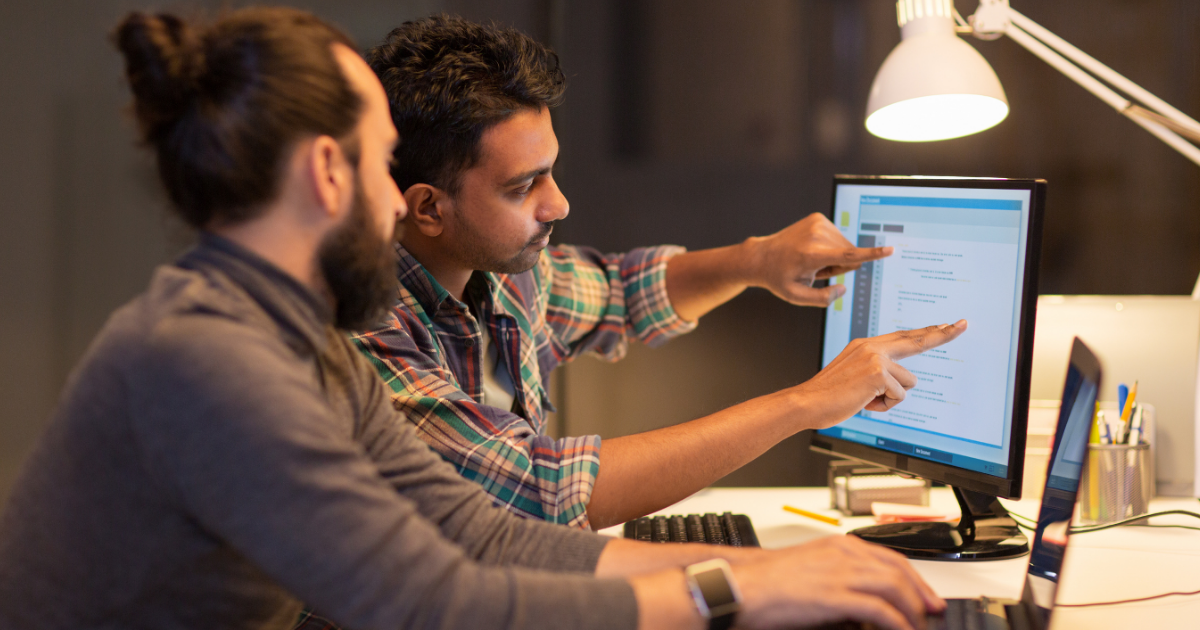 two men working at a computer and pointing at screen