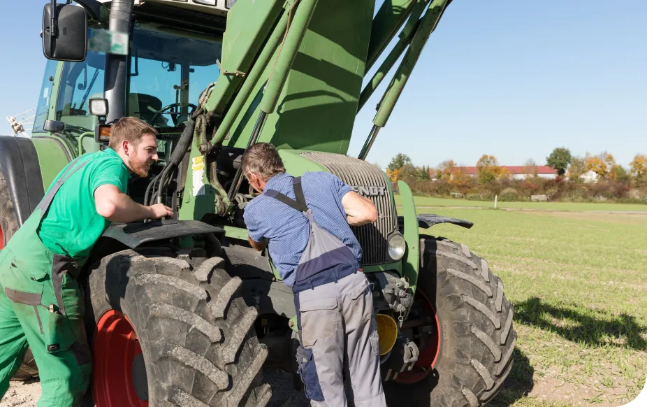 Two men in work clothes inspecting a green tractor in a field under a clear blue sky.