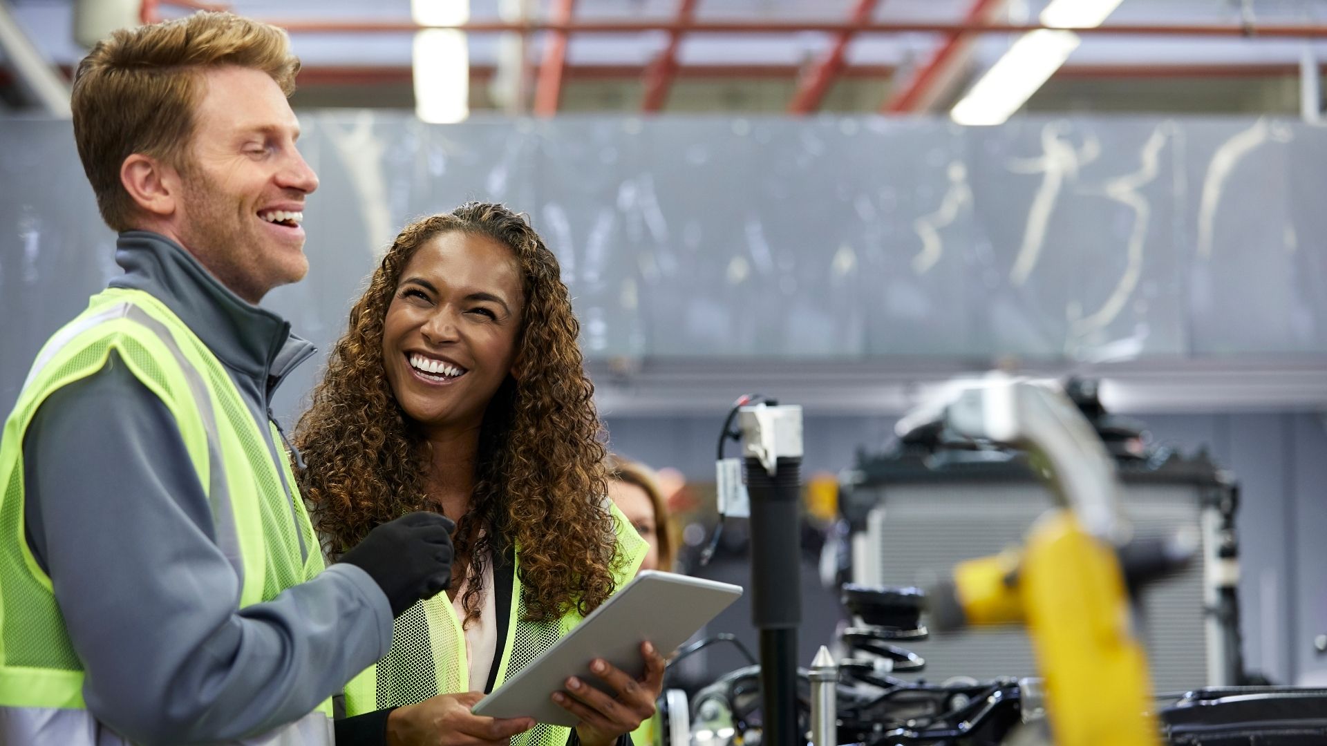 two workers in safety vests smiling and laughing while discussing something