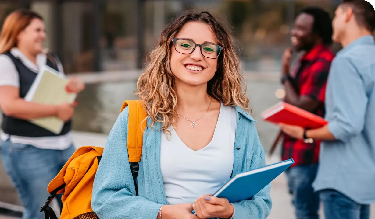 Smiling woman with glasses holds a blue folder, standing outdoors with a yellow backpack. Three people chat in the blurred background.