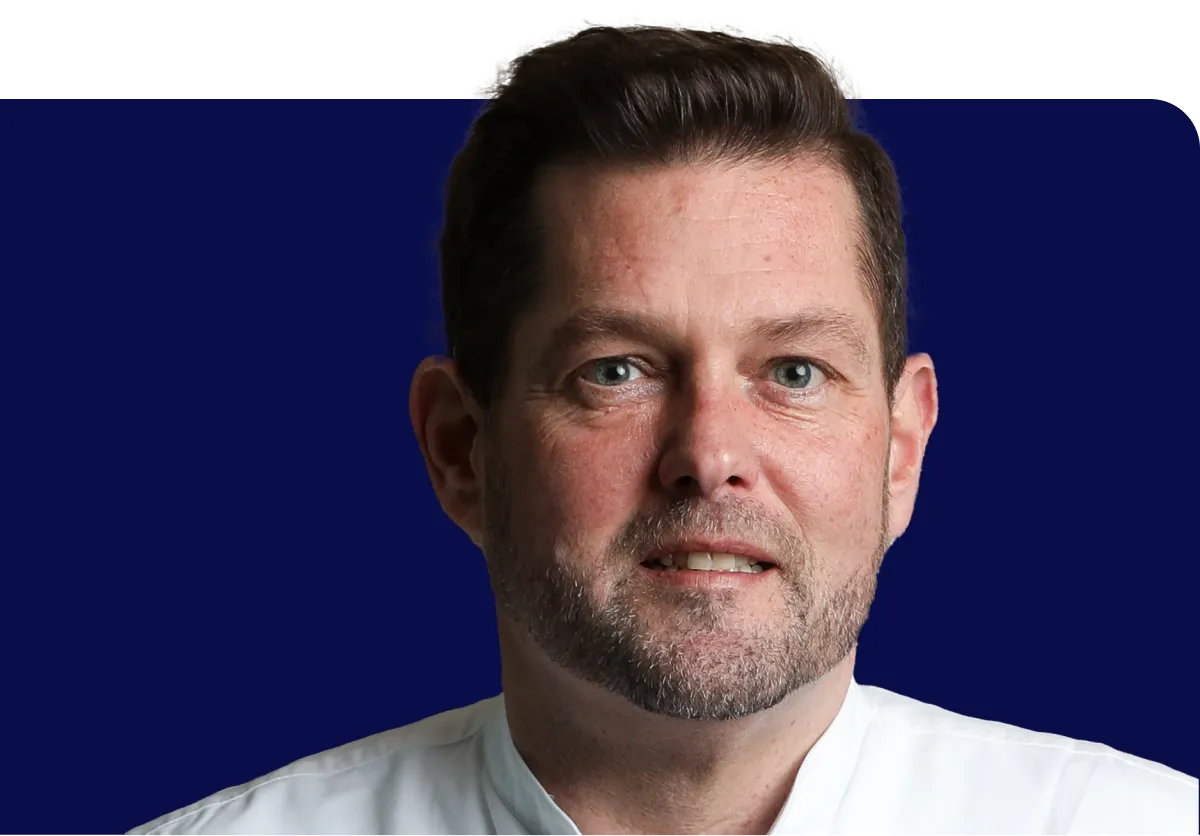 Man with short hair and beard in a white shirt, against a dark blue background.