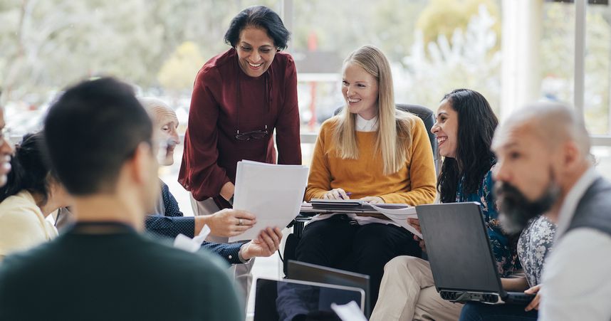 Gruppe Menschen sitzt im Kreis mit Laptops bei einem erfolgreichen Meeting