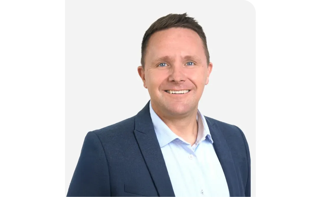 Smiling man in a blue suit and light blue shirt against a plain white background.