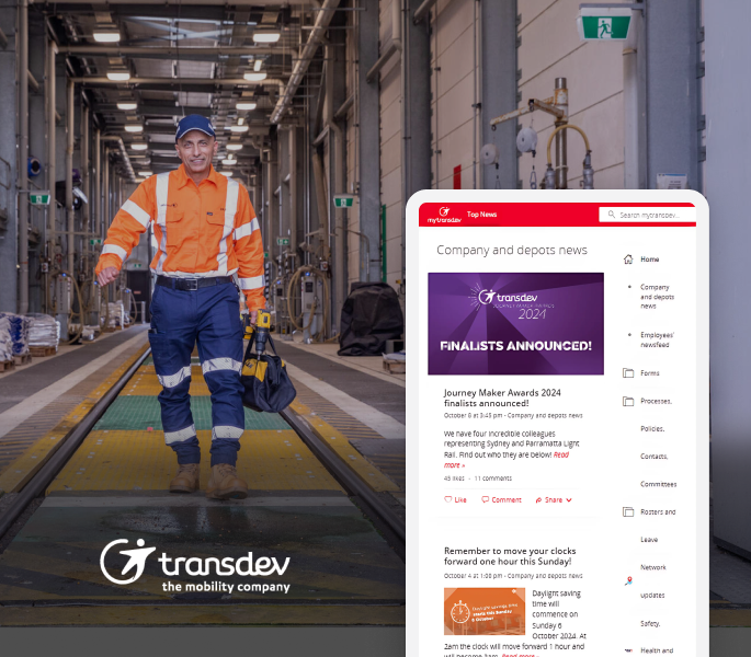 Man in safety gear walking in a depot; Transdev logo and company news displayed on a digital screen.