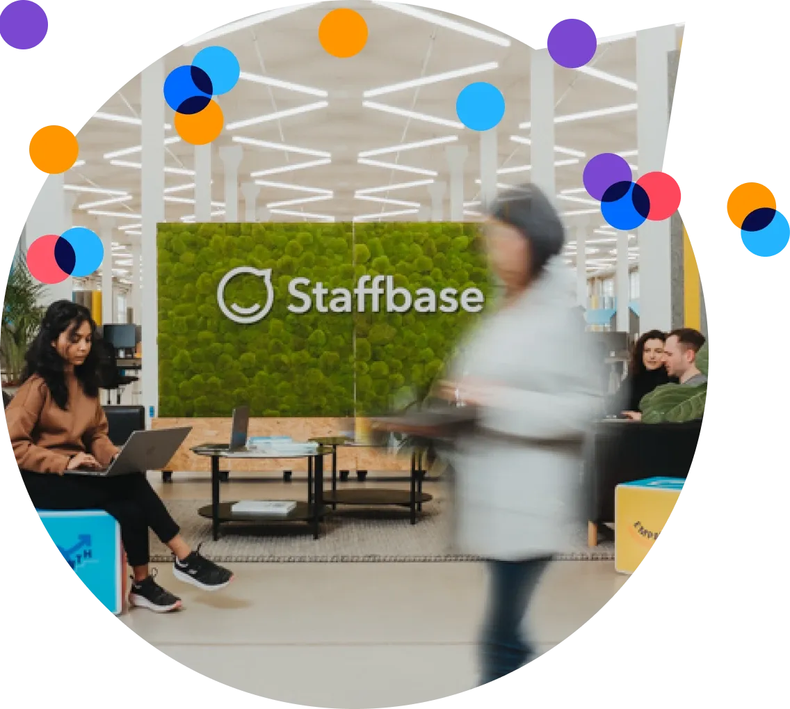 Modern office lobby with a green wall displaying "Staffbase." People are sitting and walking, some using laptops. Bright, colorful circles overlay.