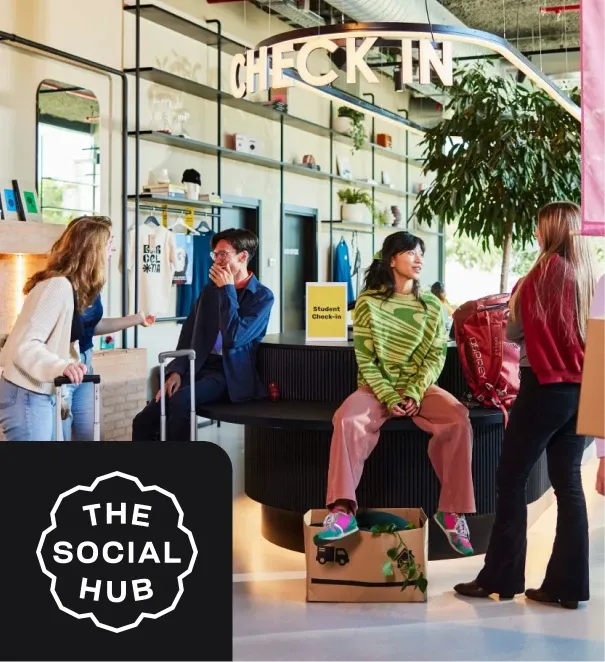 People with luggage chatting at a modern check-in area of "The Social Hub," featuring a large plant and stylish decor.