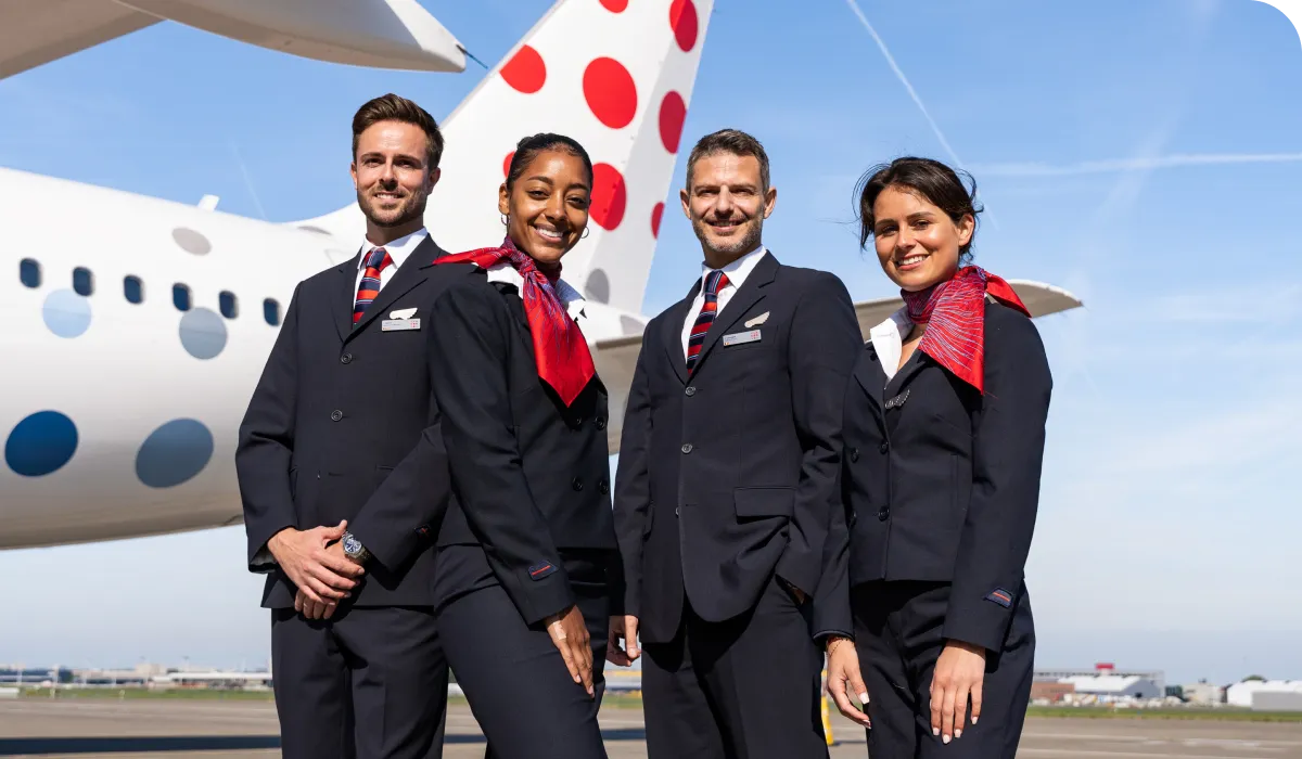 Four flight attendants in uniform stand smiling in front of an airplane.