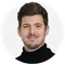Portrait of a men with brown hair. He wears a black turtle neck sweater and is smiling into the camera.