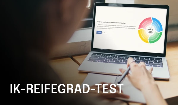 Person writing on paper with a laptop displaying a "Comms Maturity Assessment" diagram, featuring a colorful circular chart.
