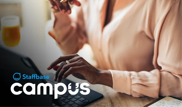 Person typing on a laptop with a notepad nearby. The text "Staffbase Campus" is visible in the foreground.