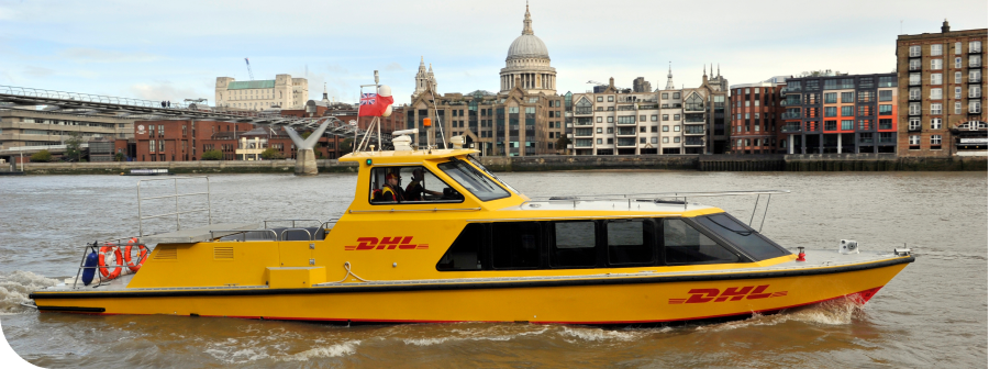 A yellow DHL boat travels on the Thames River in London, with St. Paul's Cathedral and city buildings in the background.