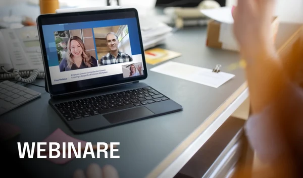 Laptop on a desk showing a webinar with two smiling speakers. The screen displays "WEBINARS" in bold text.