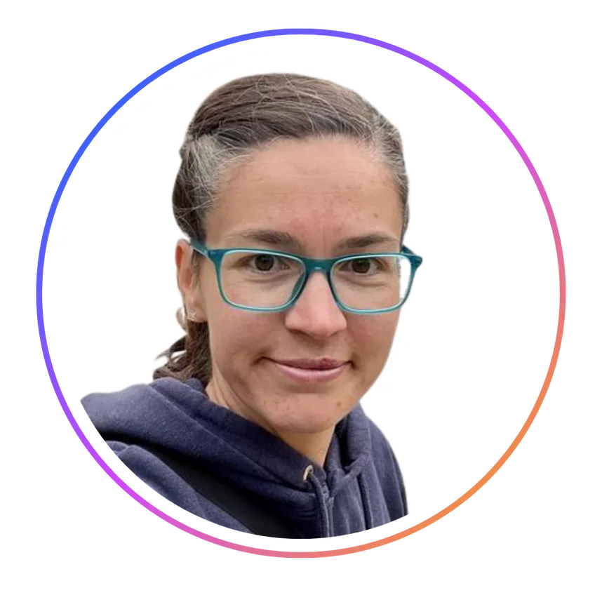 Person with glasses and dark hair tied back, wearing a navy hoodie, inside a circular frame with a gradient border, on a white background.