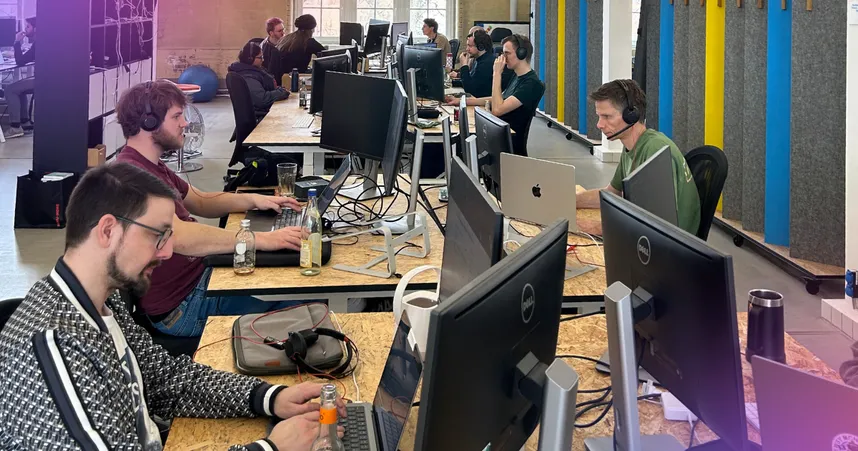 Staffbase team members collaborating at desks with dual monitors in an open-plan office during a hackathon.