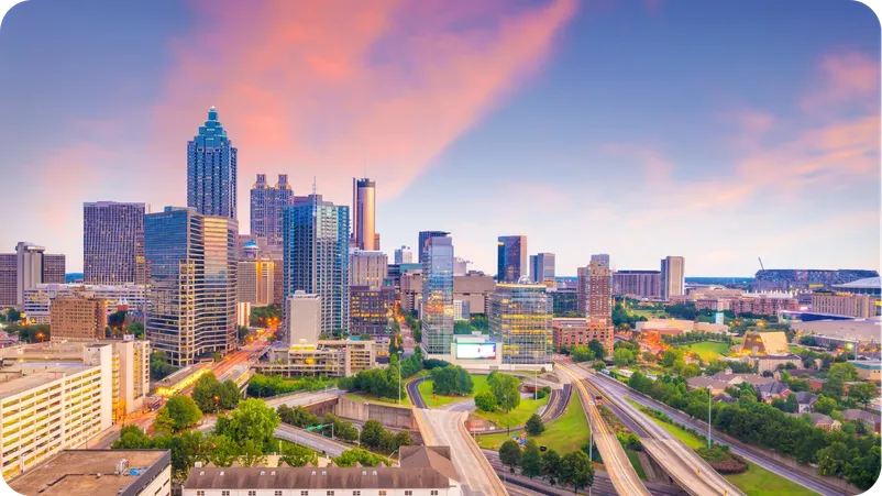 Atlanta skyline at dusk with pink clouds and illuminated highrises, including the Bank of America Plaza tower.
