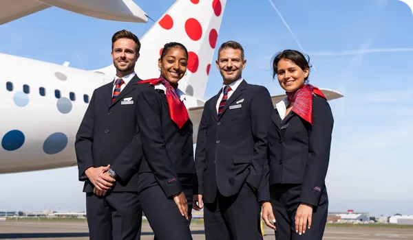 Four flight attendants in uniform stand smiling in front of an airplane.