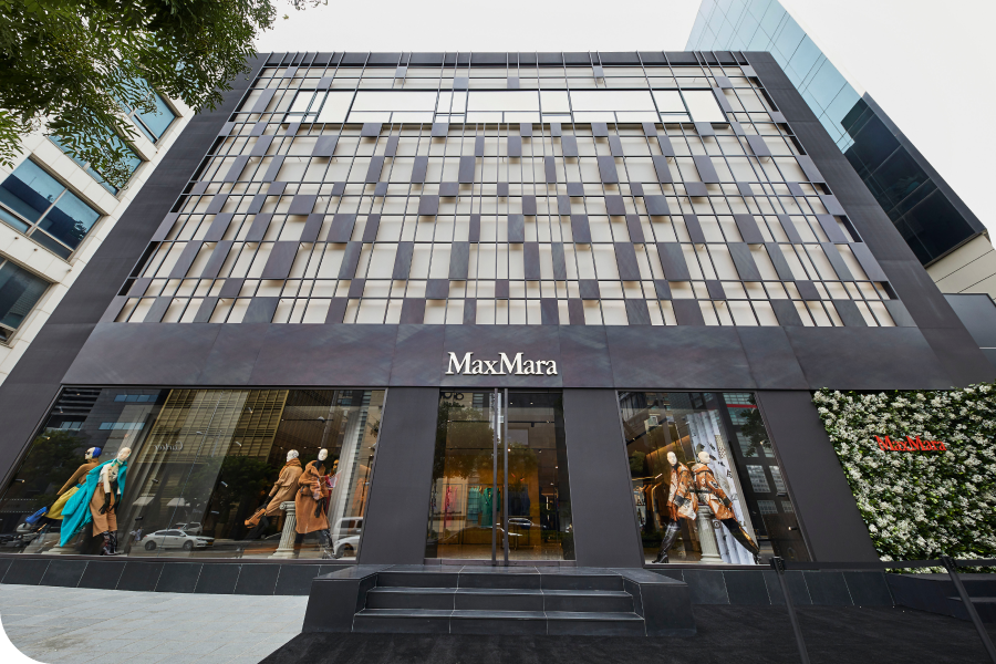 Exterior of a Max Mara store with mannequins in the window displays and a modern, geometric facade.
