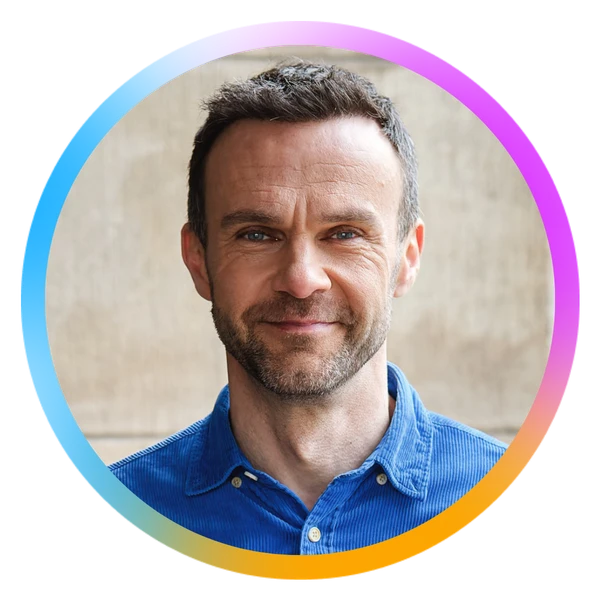 Smiling man with short hair and a beard wearing a blue shirt, framed by a colorful circular border.