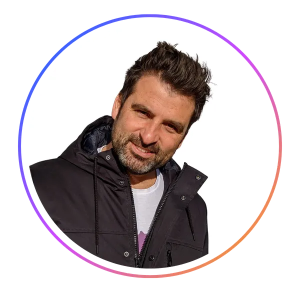 Man with dark hair and beard, wearing a black jacket, smiling at the camera. Circular frame with a gradient border.