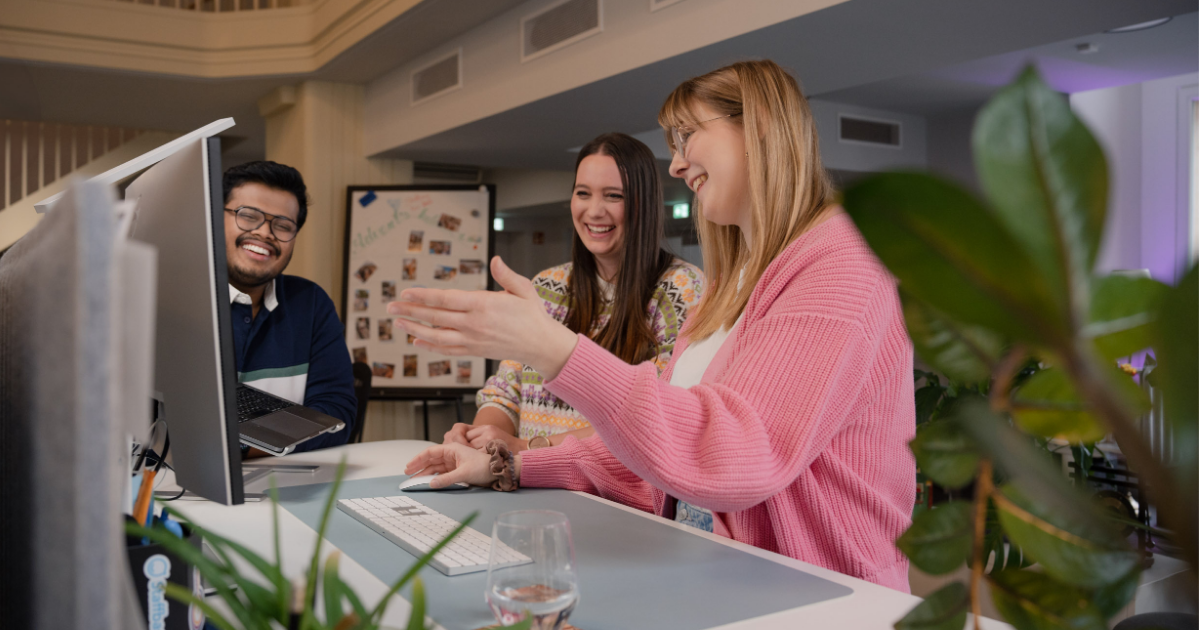 three people smile and gesture at computer