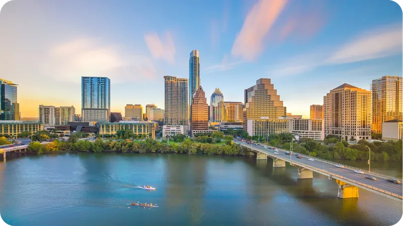 Austin, Texas skyline at sunset along Lady Bird Lake, with rowers and a bridge in the foreground.