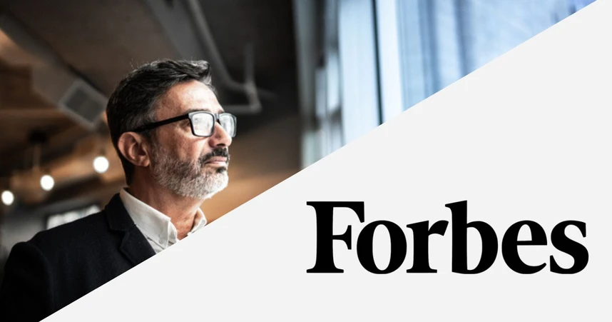 Man in glasses and suit looking out window in a modern office setting, with the Forbes logo in the foreground.